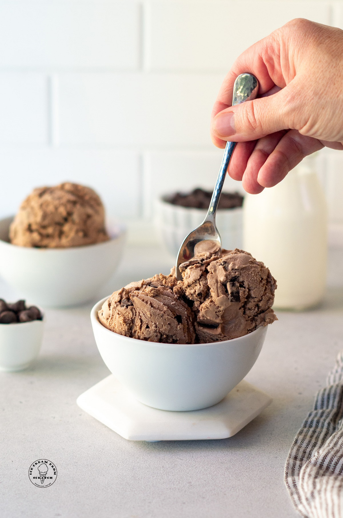 a person eating a bowl of chocolate chocolate chip ice cream with a small silver spoon.