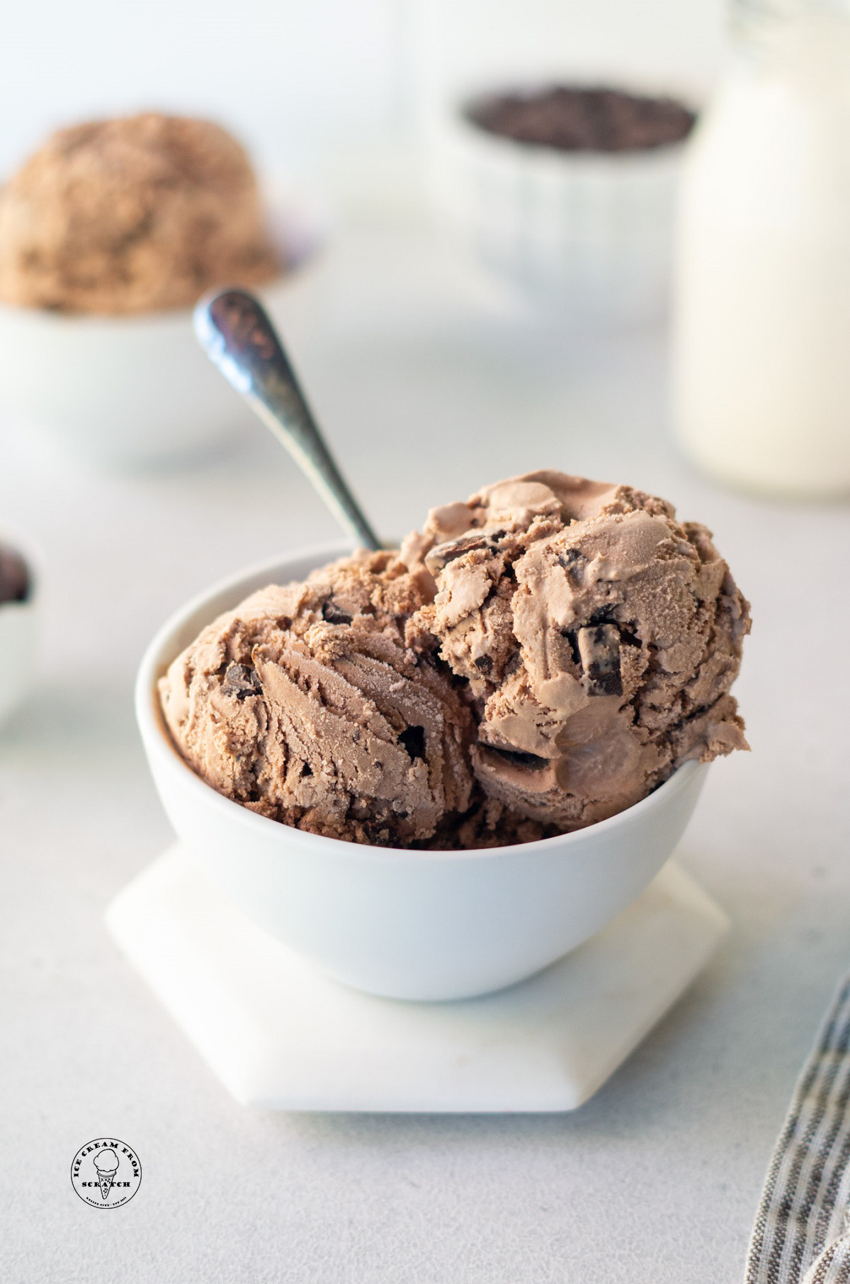 a bowl of chocolate ice cream with chocolate chunks with a spoon it in.