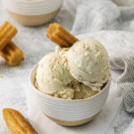 a bowl filled with scoops of cinnamon churro ice cream with a churro as garnish.