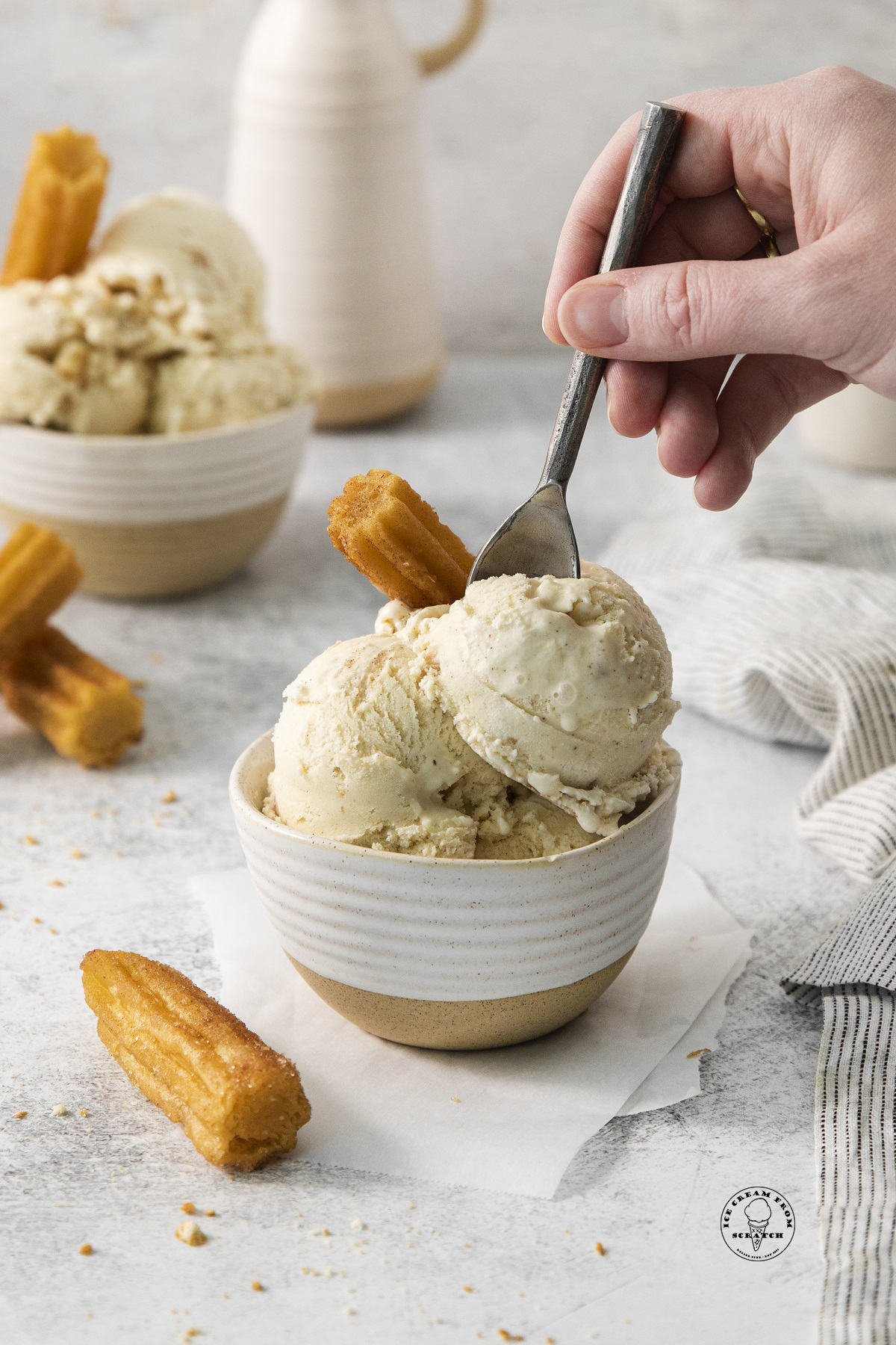 a bowl of homemade ice cream and churros. a hand is eating it with a spoon.