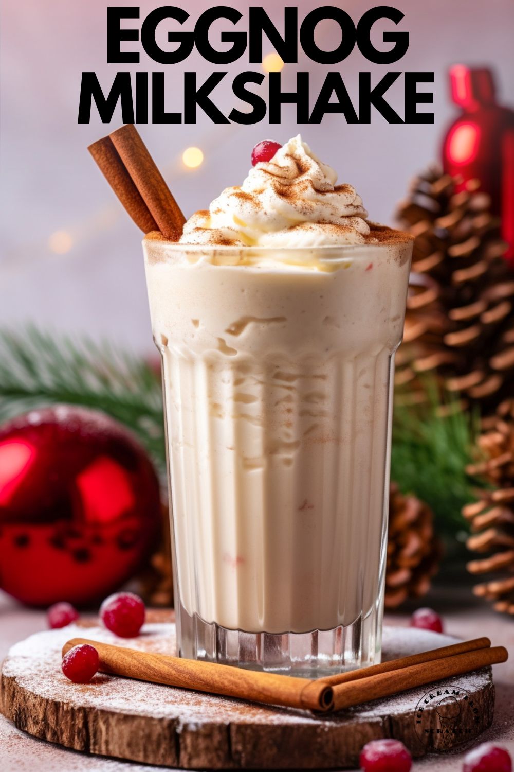 An eggnog milkshake in a tall glass, garnished with cinnamon sticks, whipped cream, and a cranberry. In the background are red ornaments, greenery, and pinecones. Text overlay says "eggnog milkshake" in capital letters"
