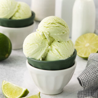 a bowl filled with scoops of lime ice cream, on a counter with fresh limes and cream