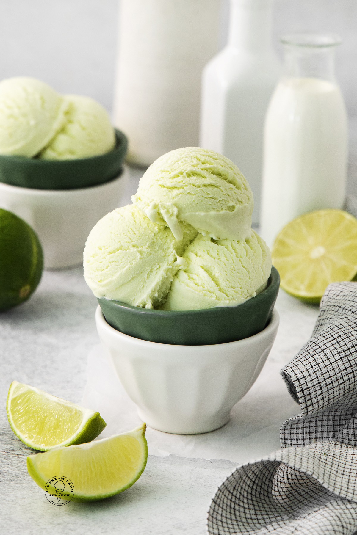 a bowl filled with scoops of lime ice cream, on a counter with fresh limes and cream
