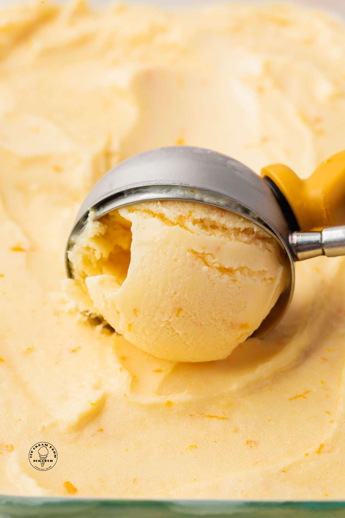 a scoop pulling up a serving of homemade creamy orange ice cream.