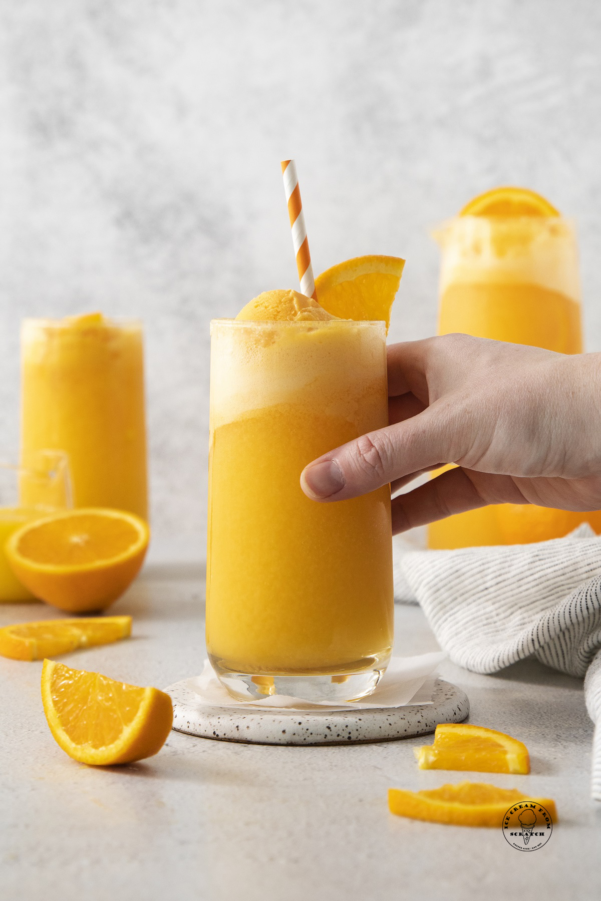 a hand picking up a glass of homemade orange sherbet punch.