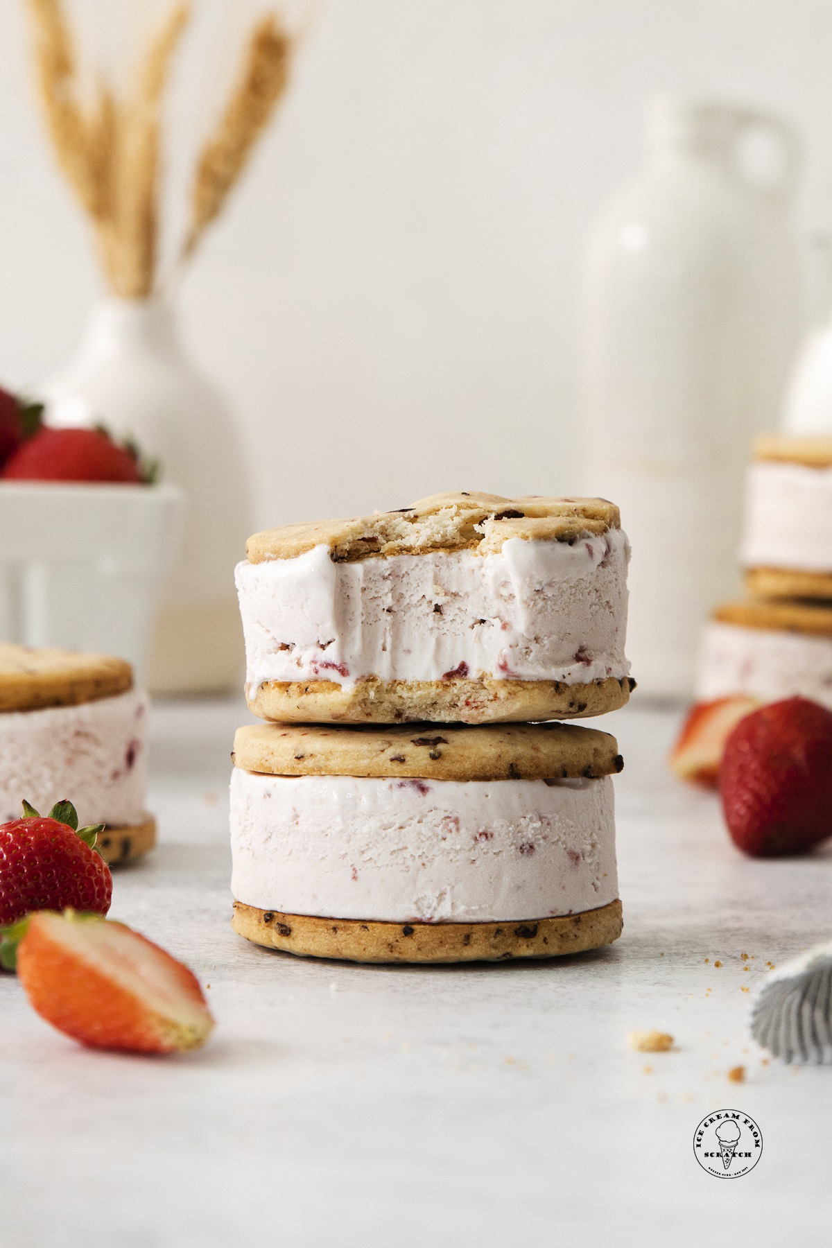 Two round cookie strawberry ice cream sandwiches on top of each other. The top one has a bite taken.