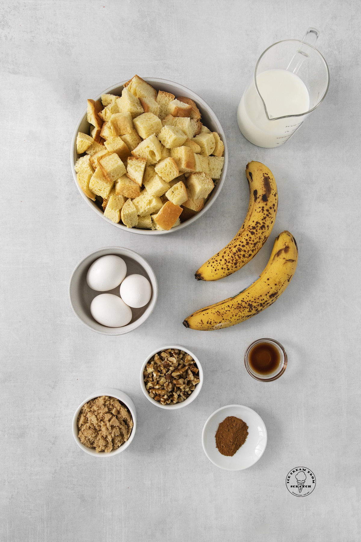 The ingredients in banana bread pudding including cubes of brioche, nuts, ripe bananas, eggs, and milk.