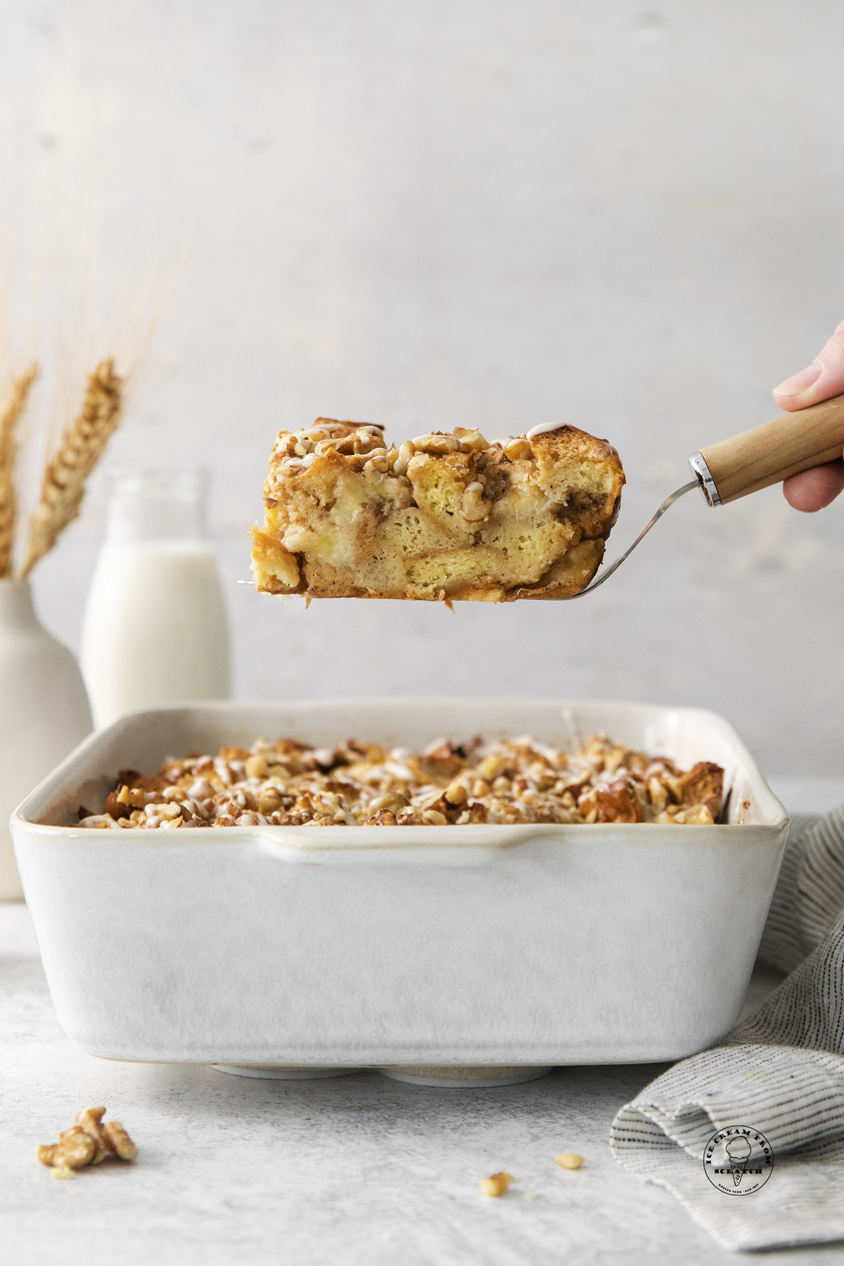 a spatula lifting out a slice of banana bread pudding topped with nuts.