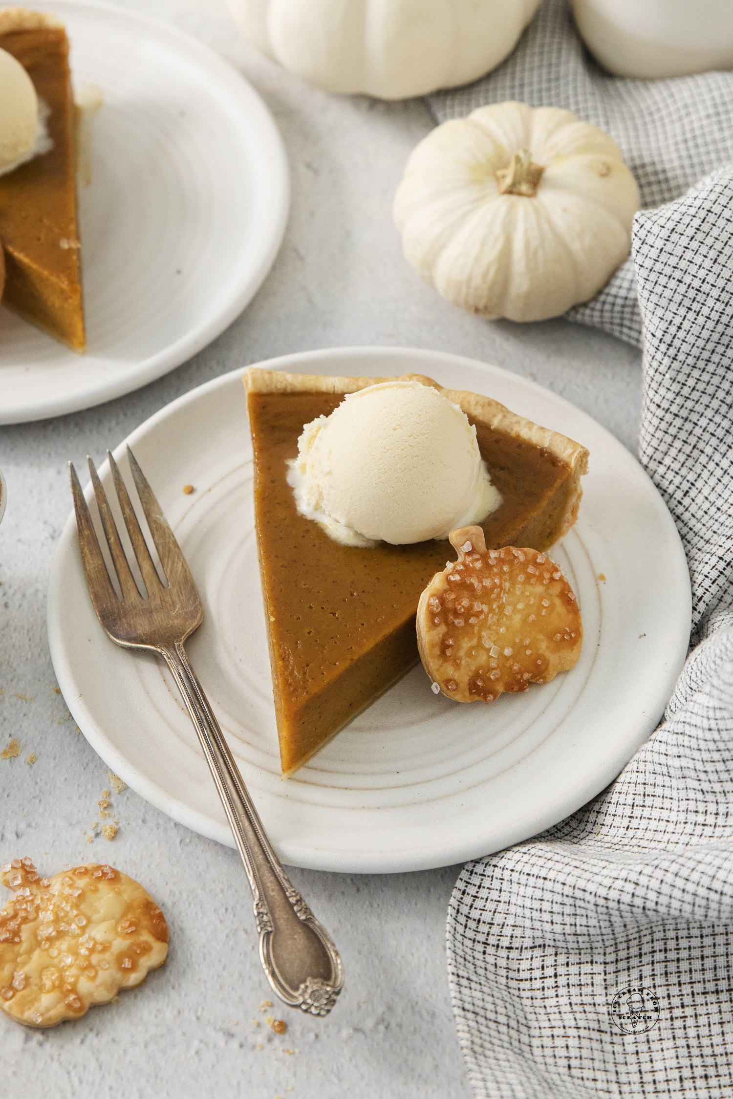 a slice of pumpkin pie with vanilla ice cream on a plate with a fork.