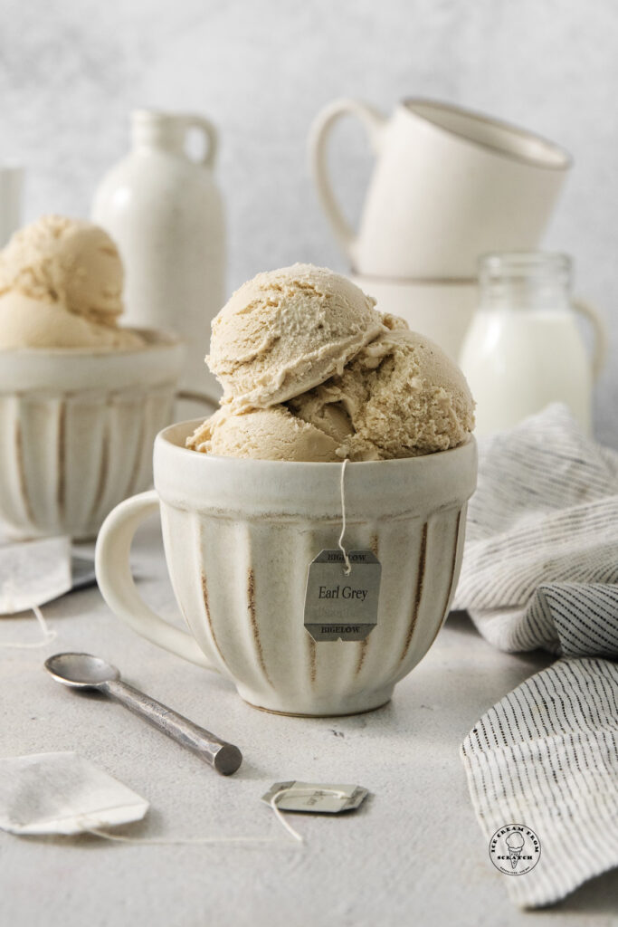 a rustic white ceramic mug on a counter, filled with scoops of earl gray ice cream. The tag from an earl gray tea bag is hanging from the mug.