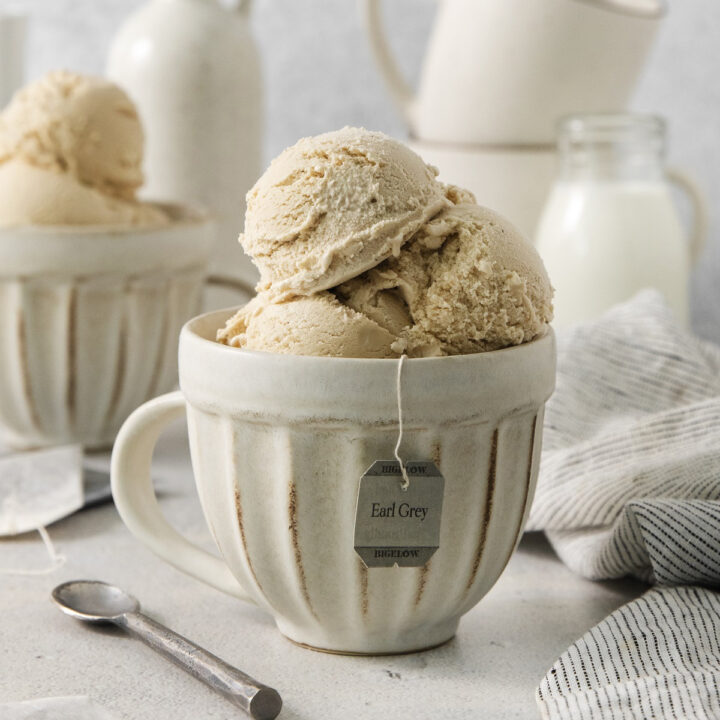 a rustic white ceramic mug on a counter, filled with scoops of earl gray ice cream. The tag from an earl gray tea bag is hanging from the mug.