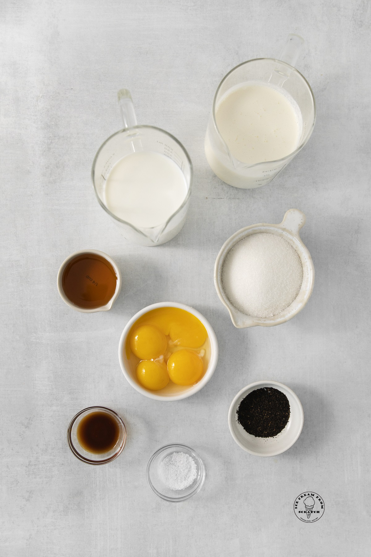 The ingredients required to make earl grey tea flavored ice cream, measured into separate bowls, arranged on a counter, and viewed from overhead.