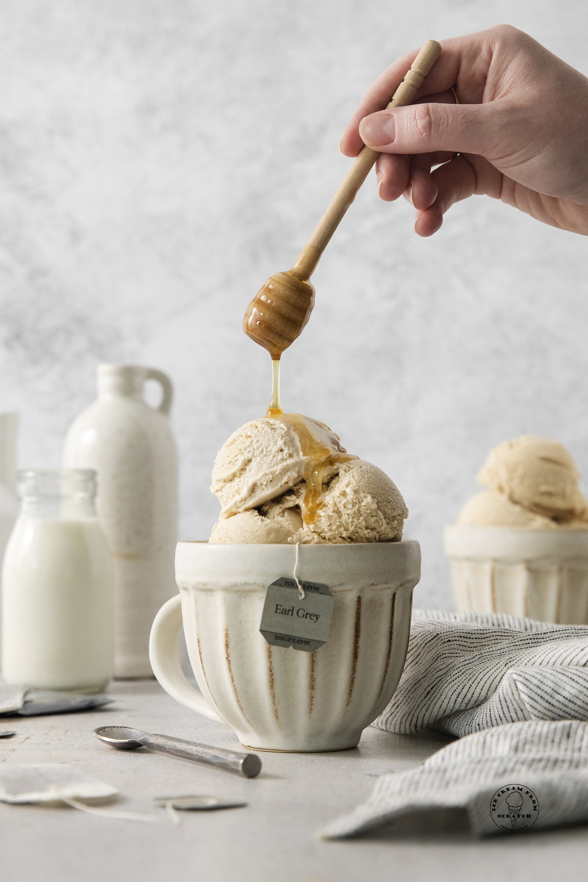 a hand holding a honey wand, drizzling honey over a mug of earl grey ice cream.
