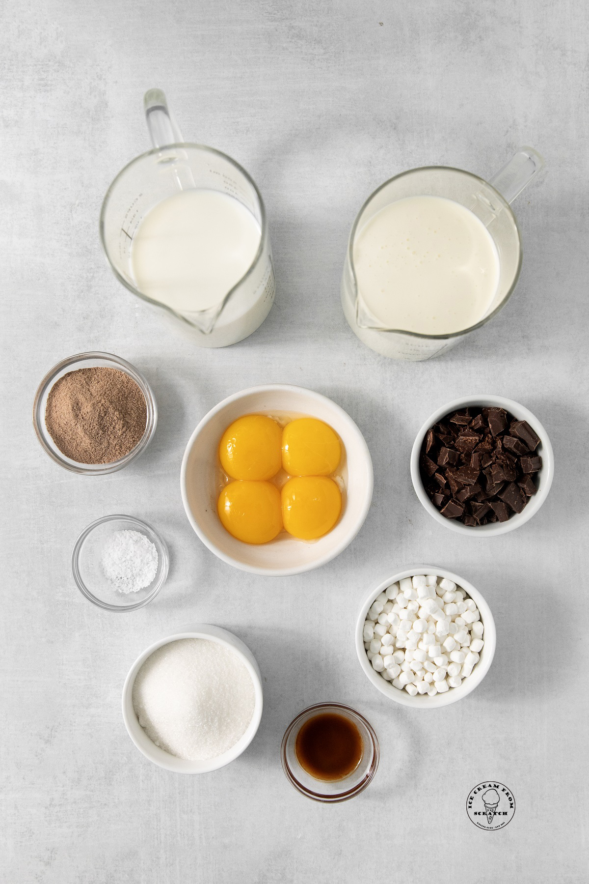 Ingredients for hot chocolate ice cream, all in separate bowls, arranged on a concrete countertop, viewed from above.