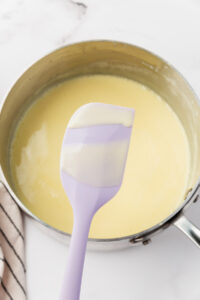 spoon showing custard is thick over a pan of custard