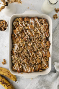 banana bread pudding mixture in a white baking dish, baked with a glaze drizzled on top
