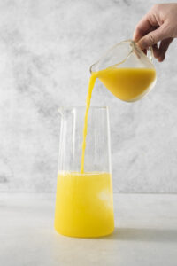 someone pouring orange juice into a drink container
