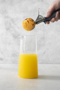 someone adding a scoop of orange sherbet to sherbet punch